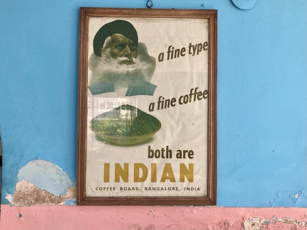 An old 1950s style poster advertising coffee hangs on a sky blue wall