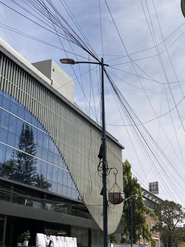 In front of a modern, glassy building, a tangled string of power lines connect to a pole.